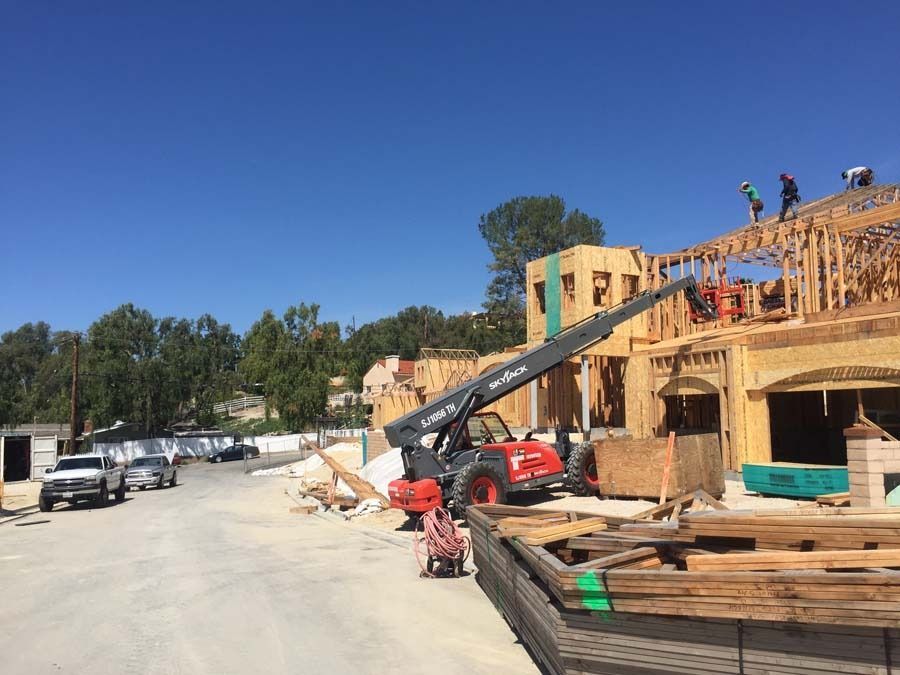 Construction workers on a building frame; telehandler lifts materials. Blue sky, sunny day.