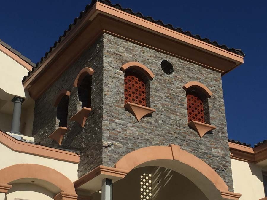 Stone-faced building with arched windows, tan trim, and a blue sky background.