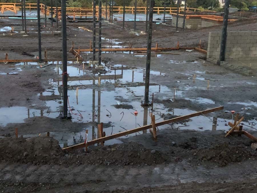 Construction site with puddles reflecting steel beams and muddy ground.