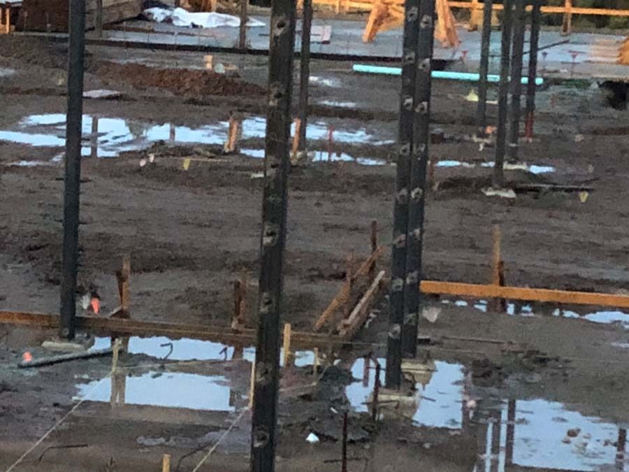 Construction site with metal pillars in wet concrete.