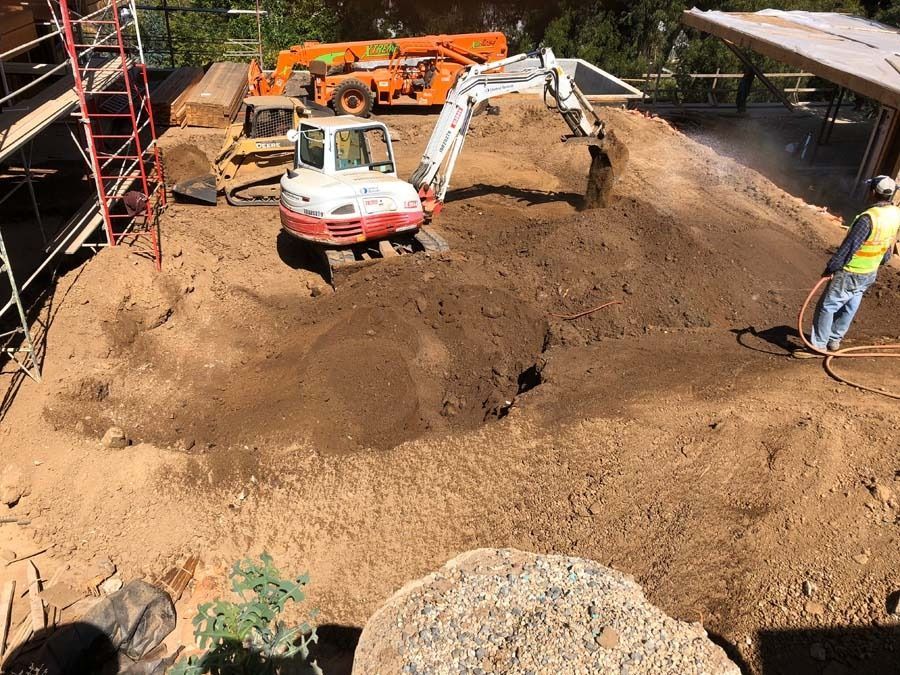 Construction site with excavator and other heavy machinery moving earth. Person on right sprays water.
