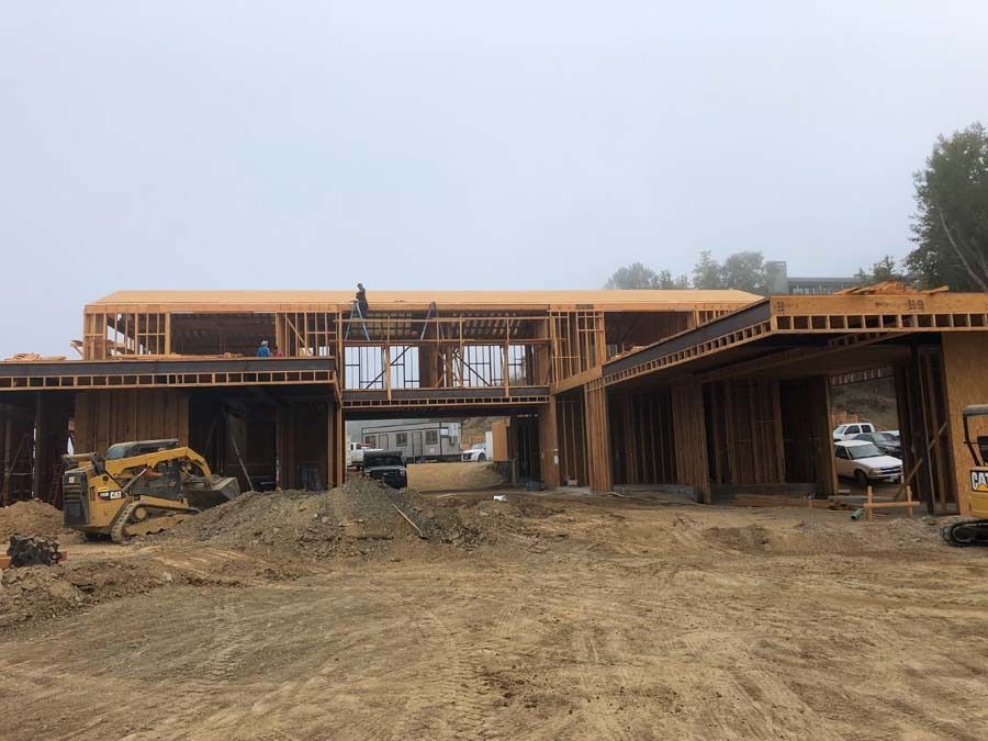 Construction site with wooden frame of a modern house, heavy machinery, and a foggy sky.