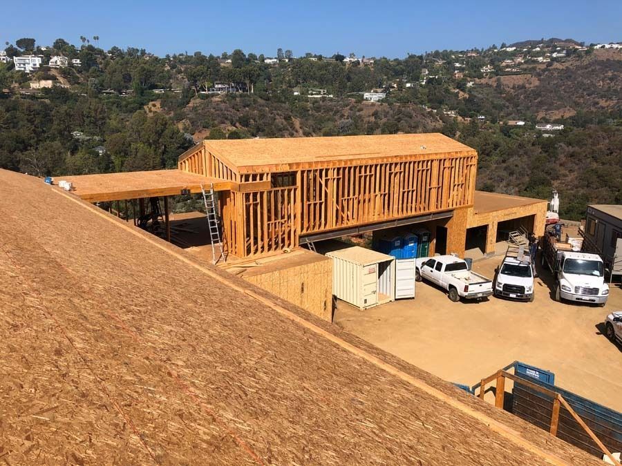 Construction site with wooden frame of a building on a hill. Cars and containers are parked.
