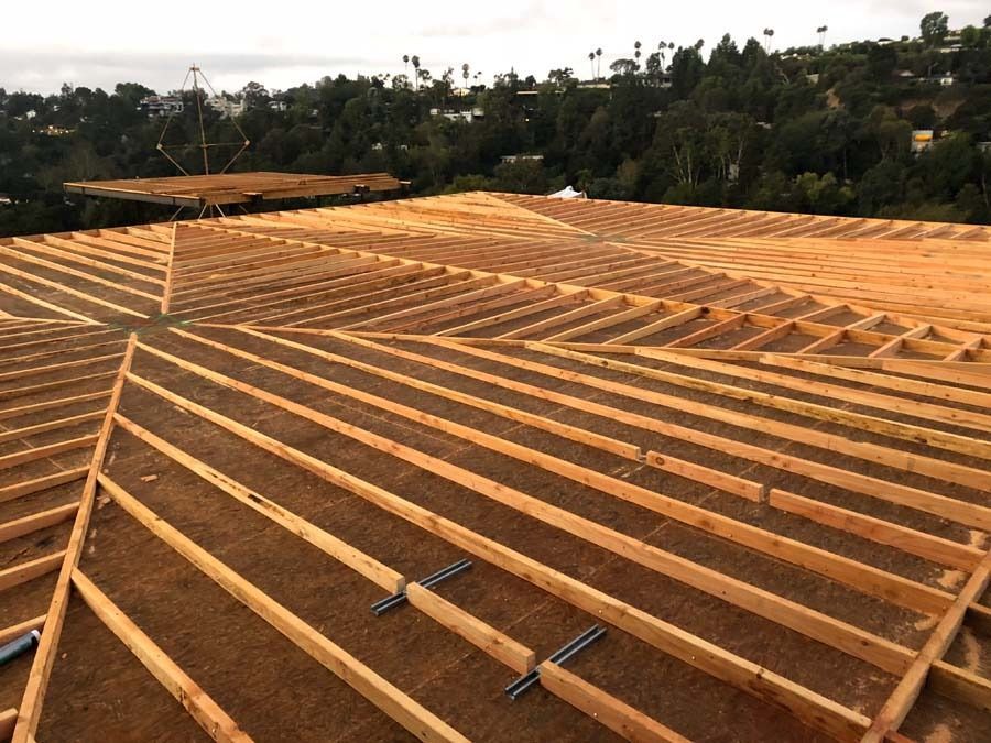 Wooden roof frame under construction, with a hillside view and green trees in the background.