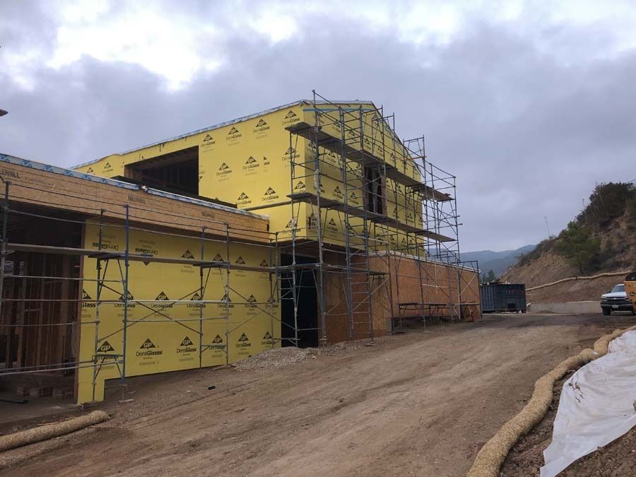 Construction site; a partially built house with yellow sheathing and scaffolding, set on a dirt road.