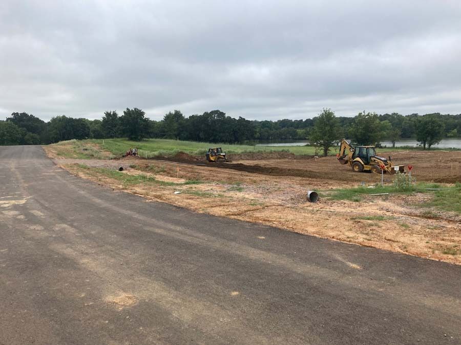 Construction site: earth-moving equipment in field, grading land near a road under cloudy sky.