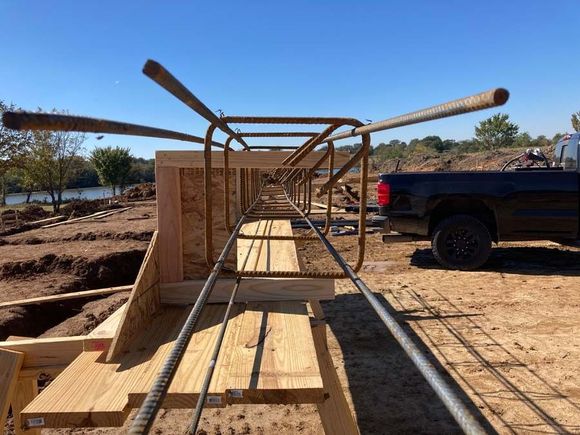 Reinforced steel rebar cage inside wooden forms, outdoor construction site with a truck.