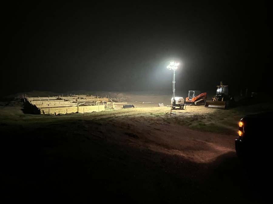 Construction site at night, floodlights illuminate equipment and circular structures.