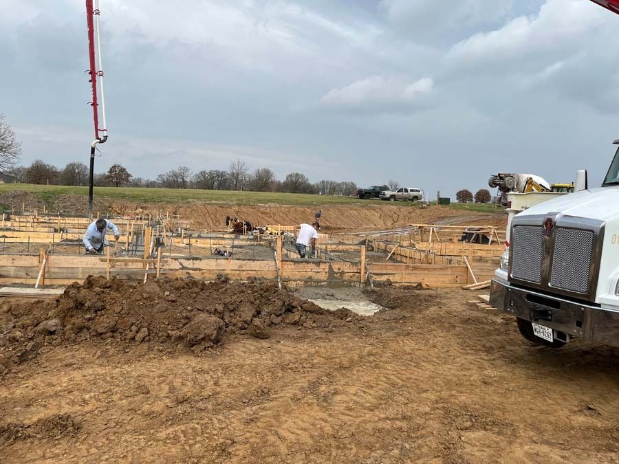 Construction workers pouring concrete into forms on a cloudy day. A concrete truck and pump are present.