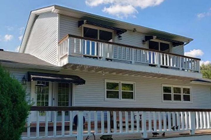 Two-story house with a deck. Light gray siding, dark awnings, and a blue sky.