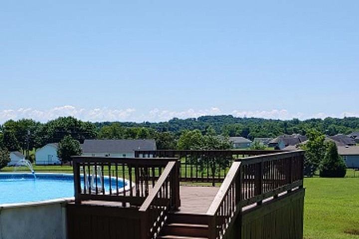 Deck overlooking a pool and a grassy yard with houses and a distant treeline under a blue sky.
