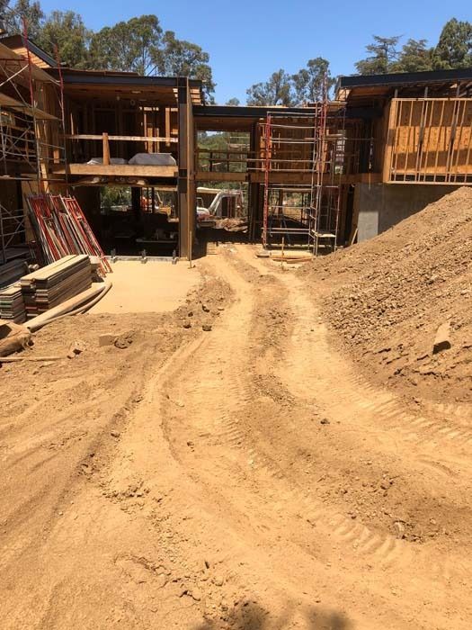 Construction site with dirt road leading to a building's wooden frame under a blue sky.