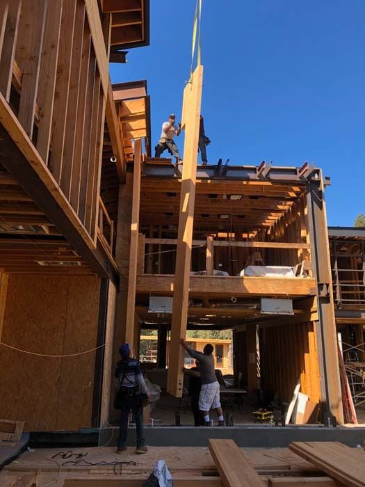 Construction workers lifting a wooden beam into a partially built multi-story building. Sunny day.