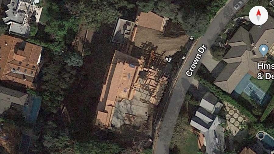Aerial view of a building under construction on Crown Dr. Brown roof and dirt with surrounding houses and trees.