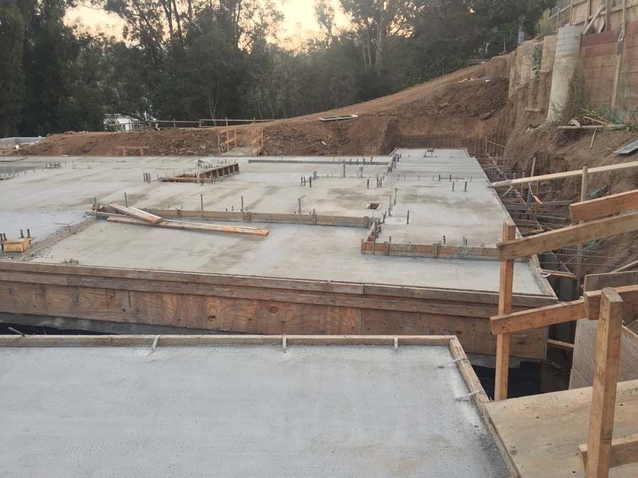 Construction site with concrete foundations, wooden forms, and earthwork in progress.