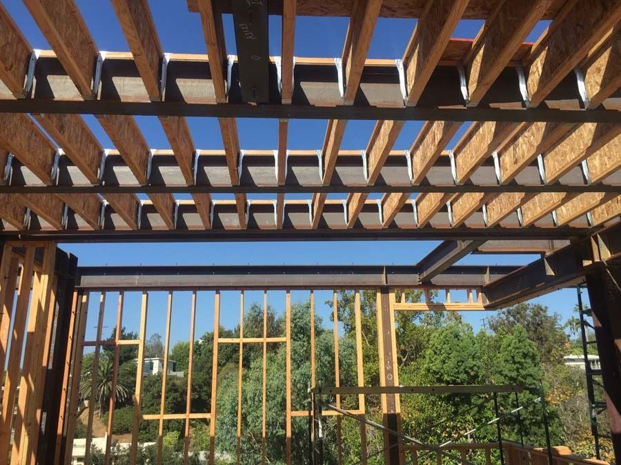 Construction framing: Wooden beams, steel girder, against a blue sky, trees visible in the background.