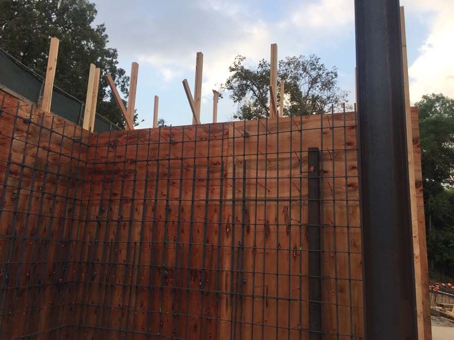 Wooden forms with rebar for a concrete wall under construction, with support beams, against a cloudy sky.