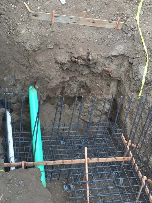 Construction site: Rebar grid, green pipe, dirt, wooden frame, and trench.