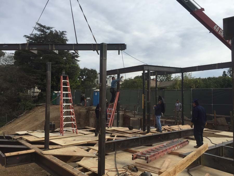 Construction site with workers installing steel beams for a building frame under a cloudy sky.