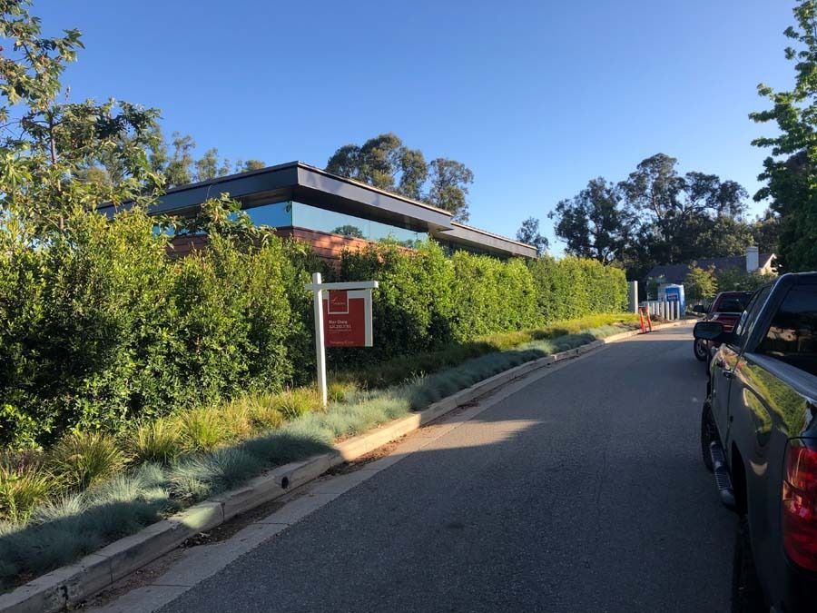 A modern building with a hedge in front. A for sale sign and a truck are visible.