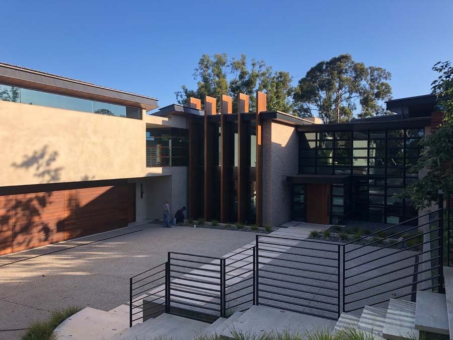Modern house with stone facade, wooden accents, and glass windows, driveway, and front steps on a sunny day.