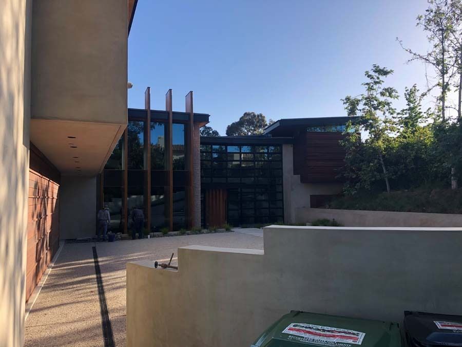 Modern house exterior with glass walls, wood accents, and a concrete patio under a blue sky.