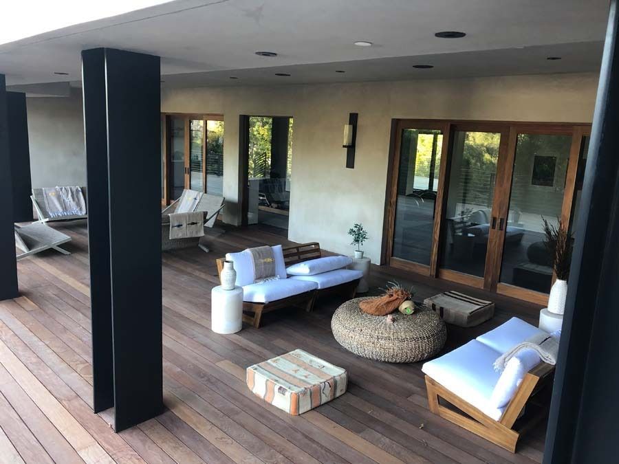 Covered outdoor patio with light wood deck, seating, and black support columns.