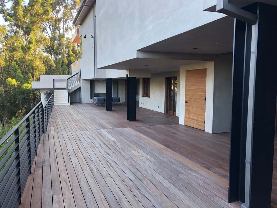 Large wooden deck on a multi-level home, black railings and support beams.