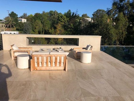 Patio with beige furniture, fireplace, and pool overlooking trees.