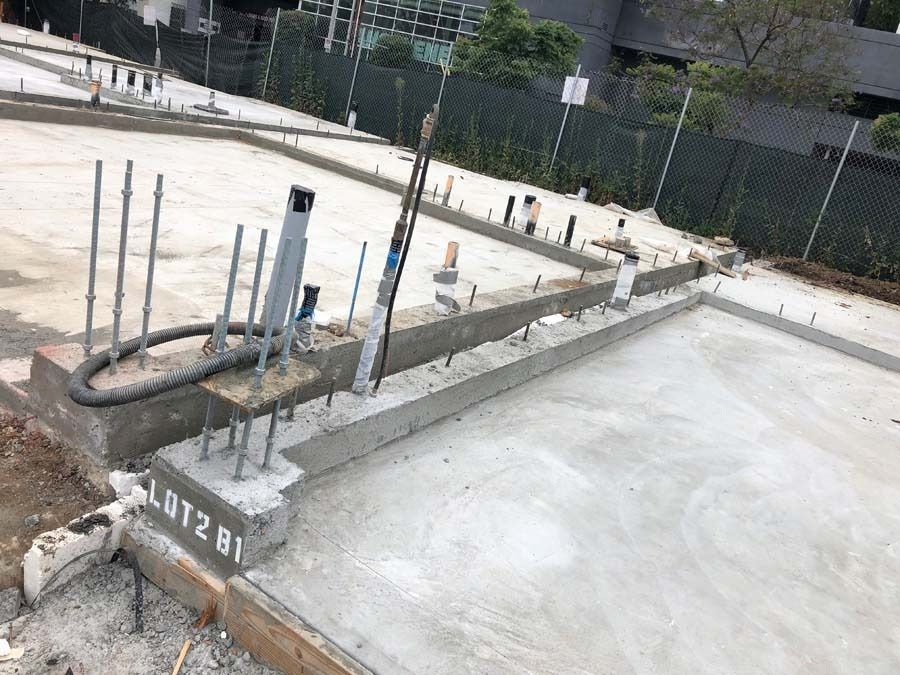 Concrete foundation under construction, with rebar and piping visible, outdoors.