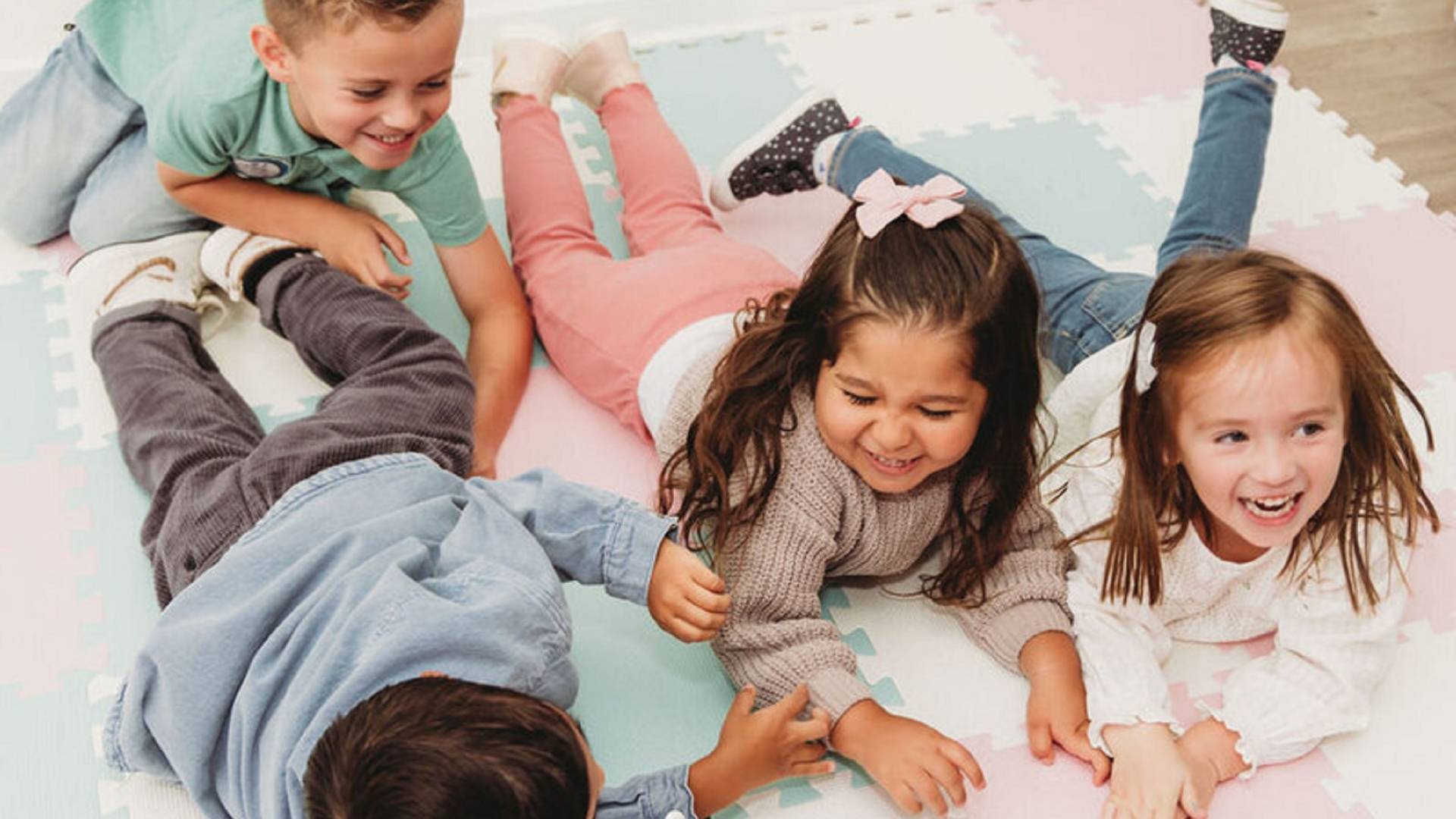 Young child with a shaved head, wearing a plaid shirt and white shirt, standing against a white brick wall.