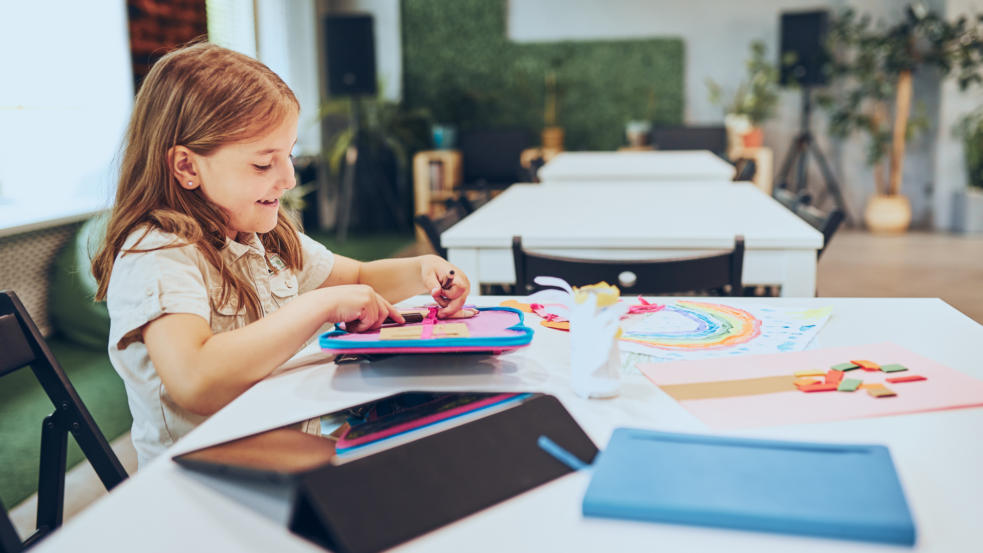 Girl creating art at a white table in a bright room with art supplies.