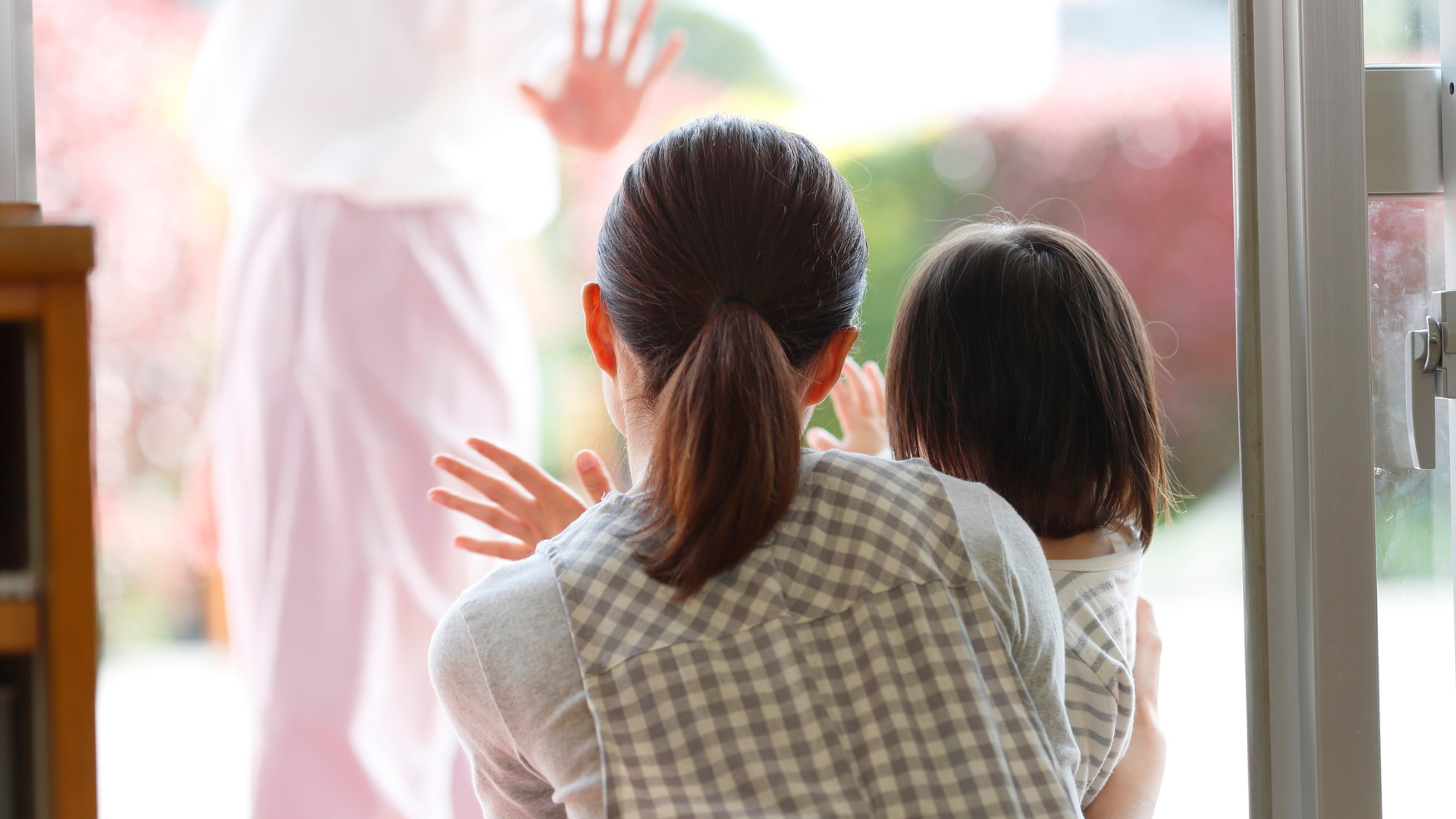 Woman and child waving goodbye through a window to another woman.