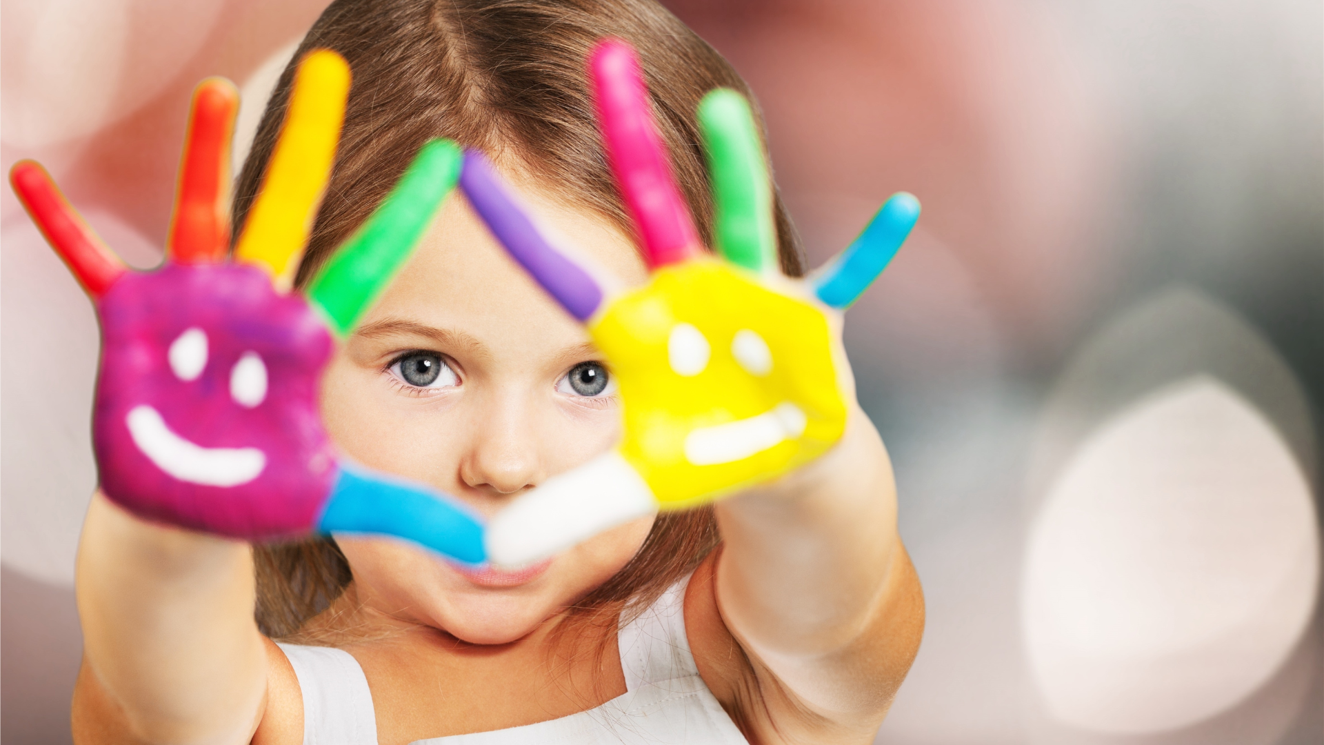 Girl with colorful paint on hands, smiling, with bokeh background.