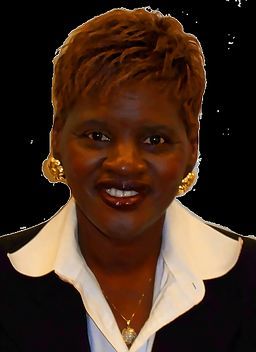 A person with short, light brown hair smiles, wearing a black blazer over a white collared shirt and gold hoop earrings.