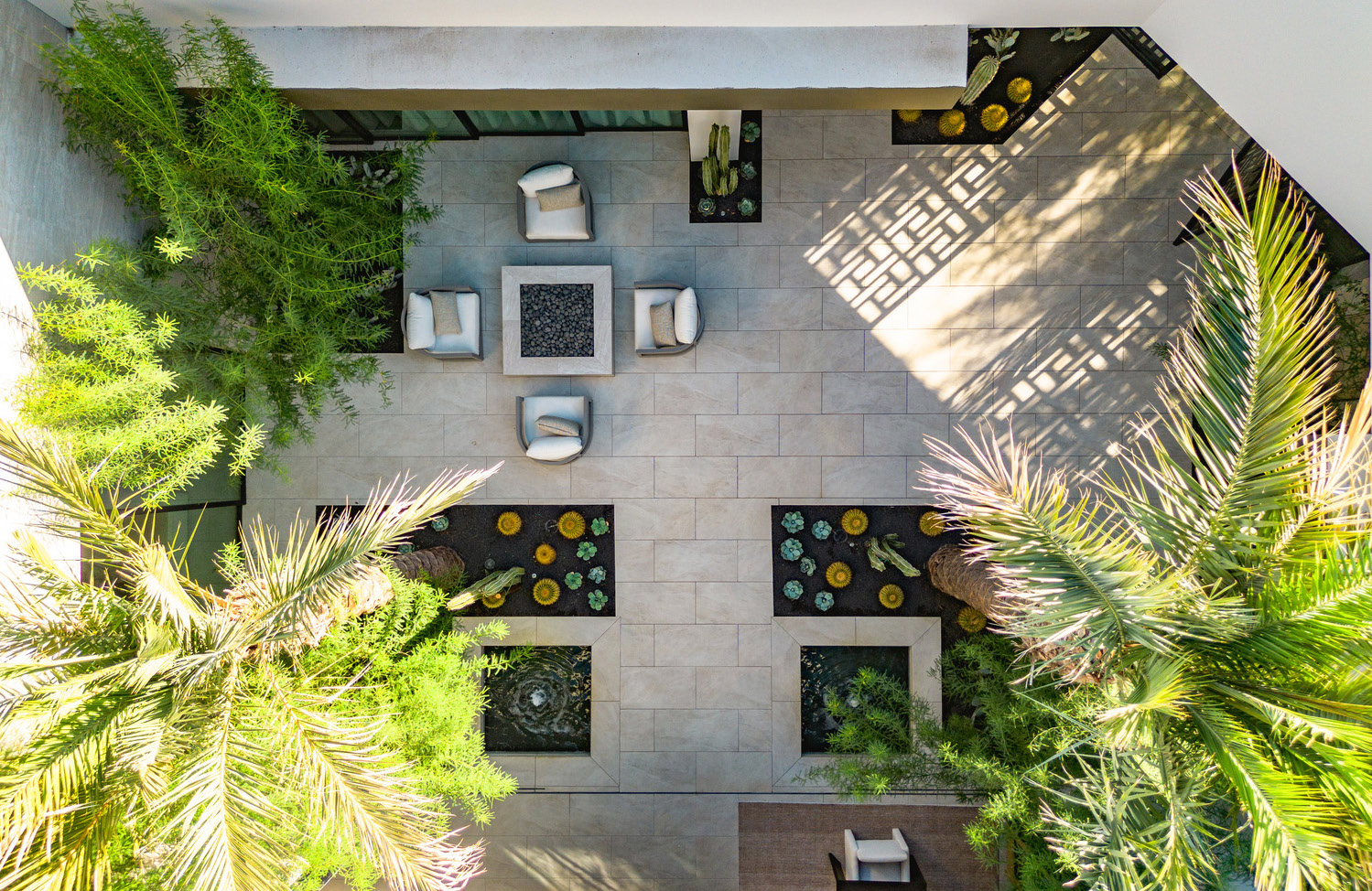 Overhead view of a modern outdoor patio with seating, fire pit, and lush green landscaping.