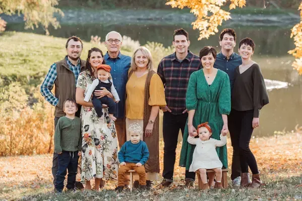 A large family is posing for a picture in front of a lake.