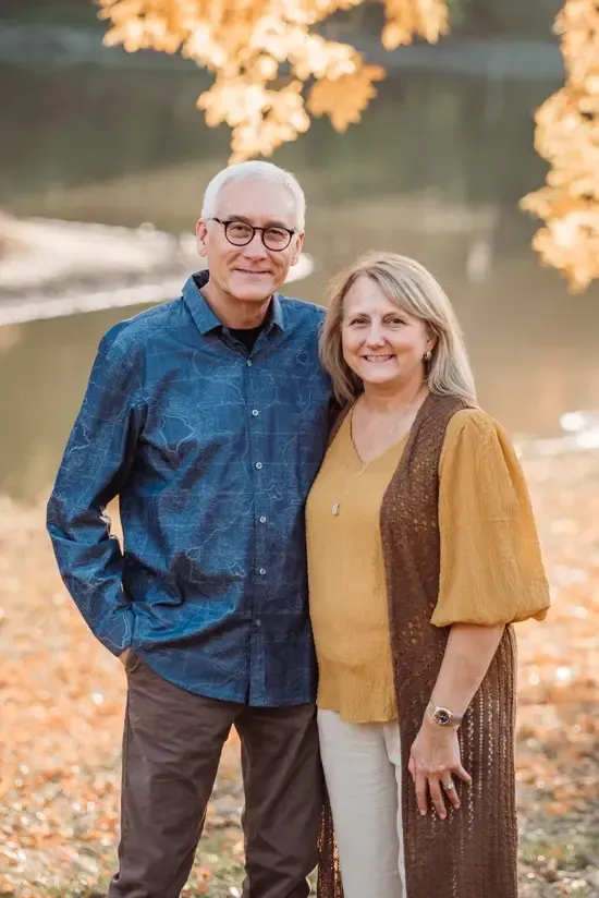 A man and a woman are posing for a picture in front of a lake.