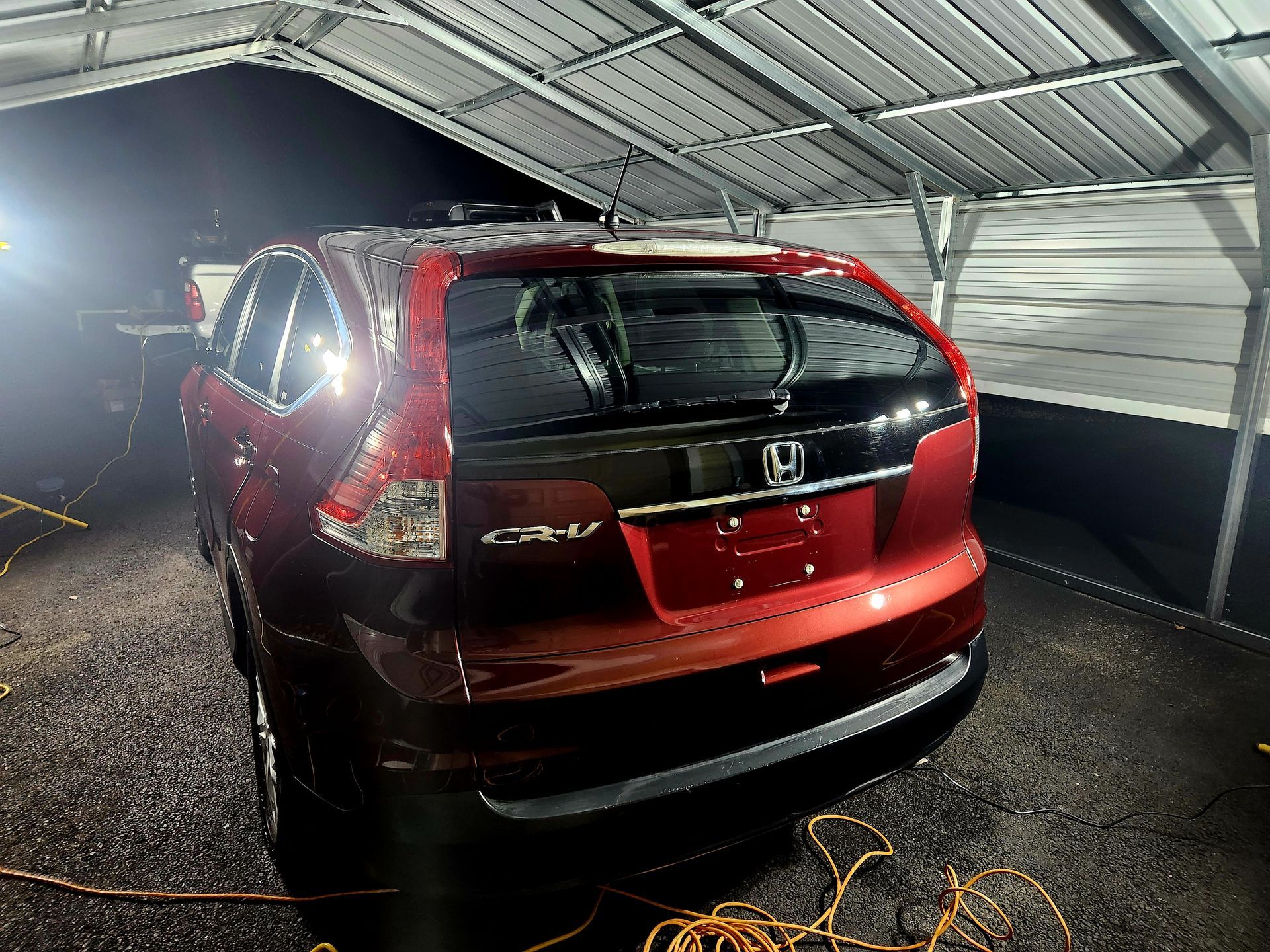 Red Honda CR-V parked under a silver carport. It's wet; likely recently washed.