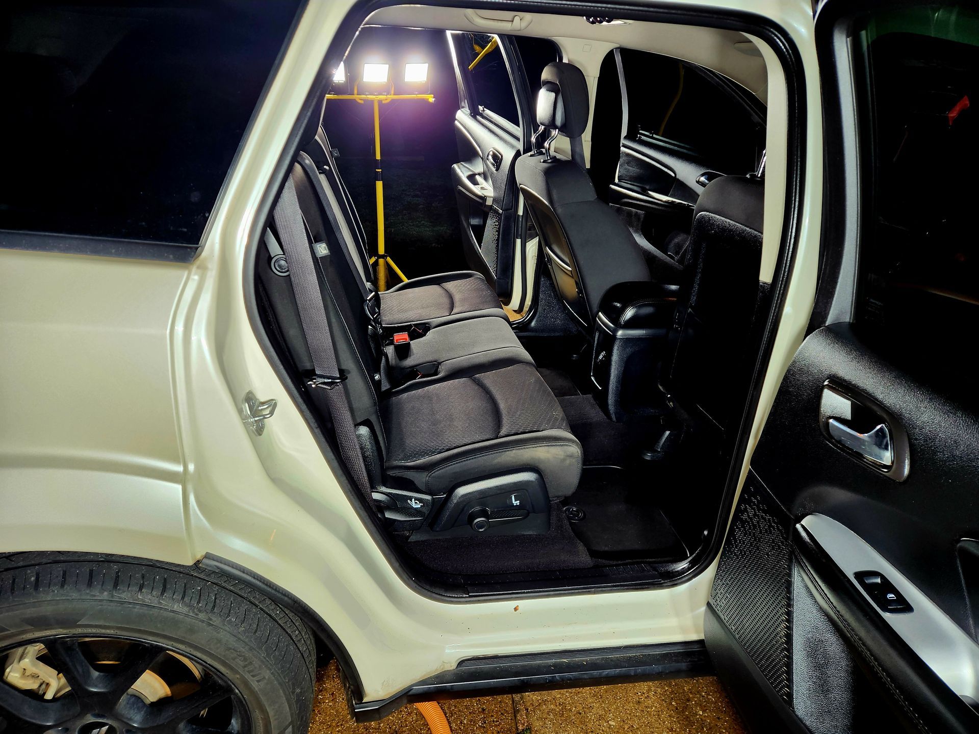 Interior of a white SUV with open door; black seats, work light, and dark windows are visible.