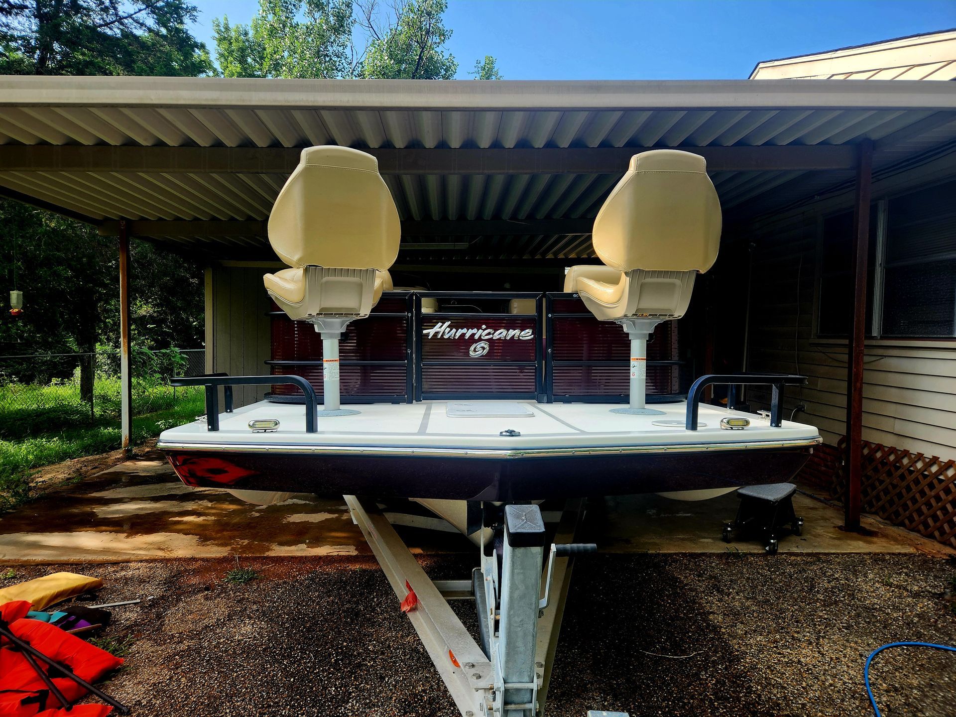 A maroon and white Hurricane HD boat on a trailer, under a carport, with two beige seats.