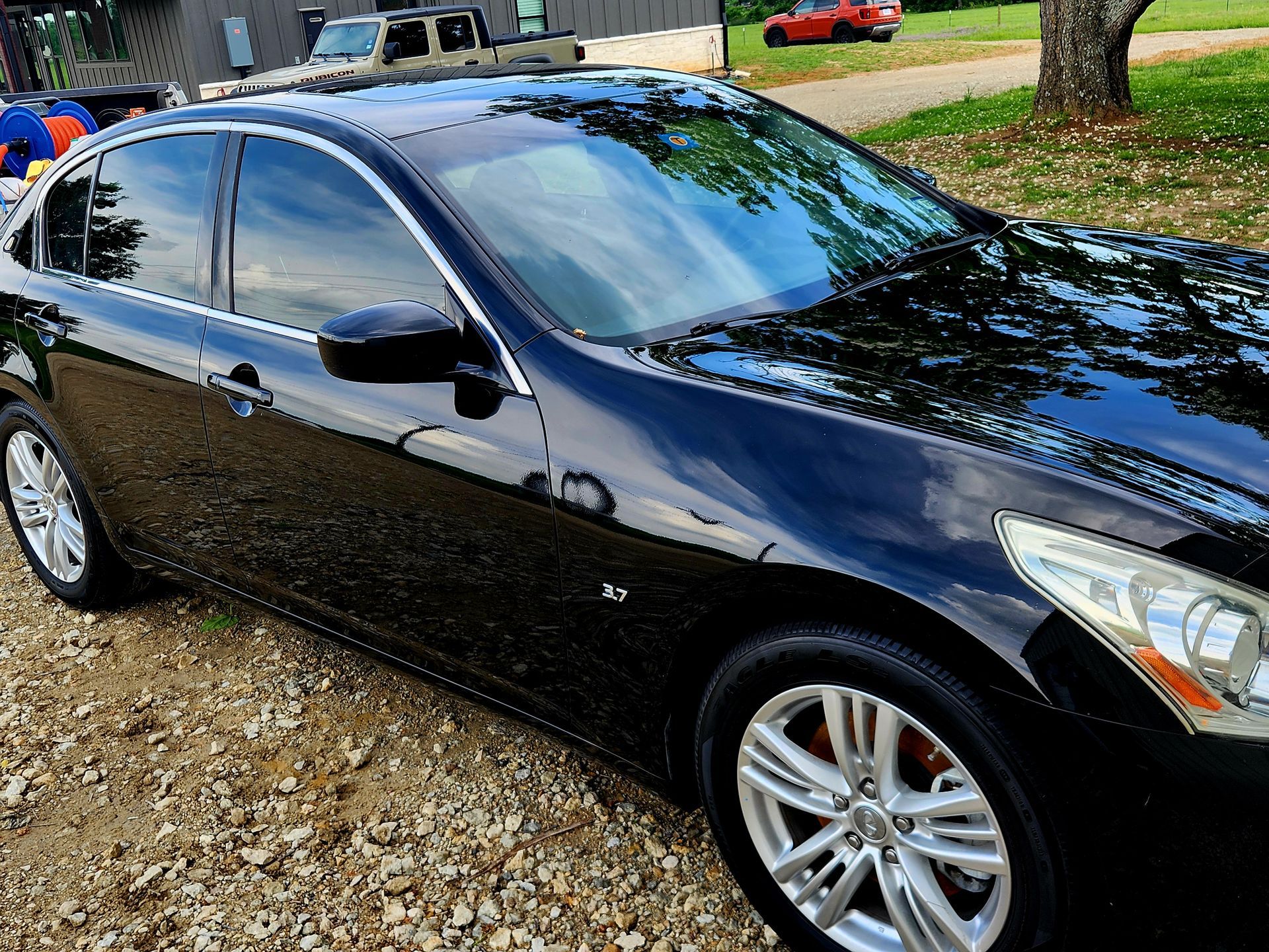 Black sedan with tinted windows parked on gravel, outdoors.