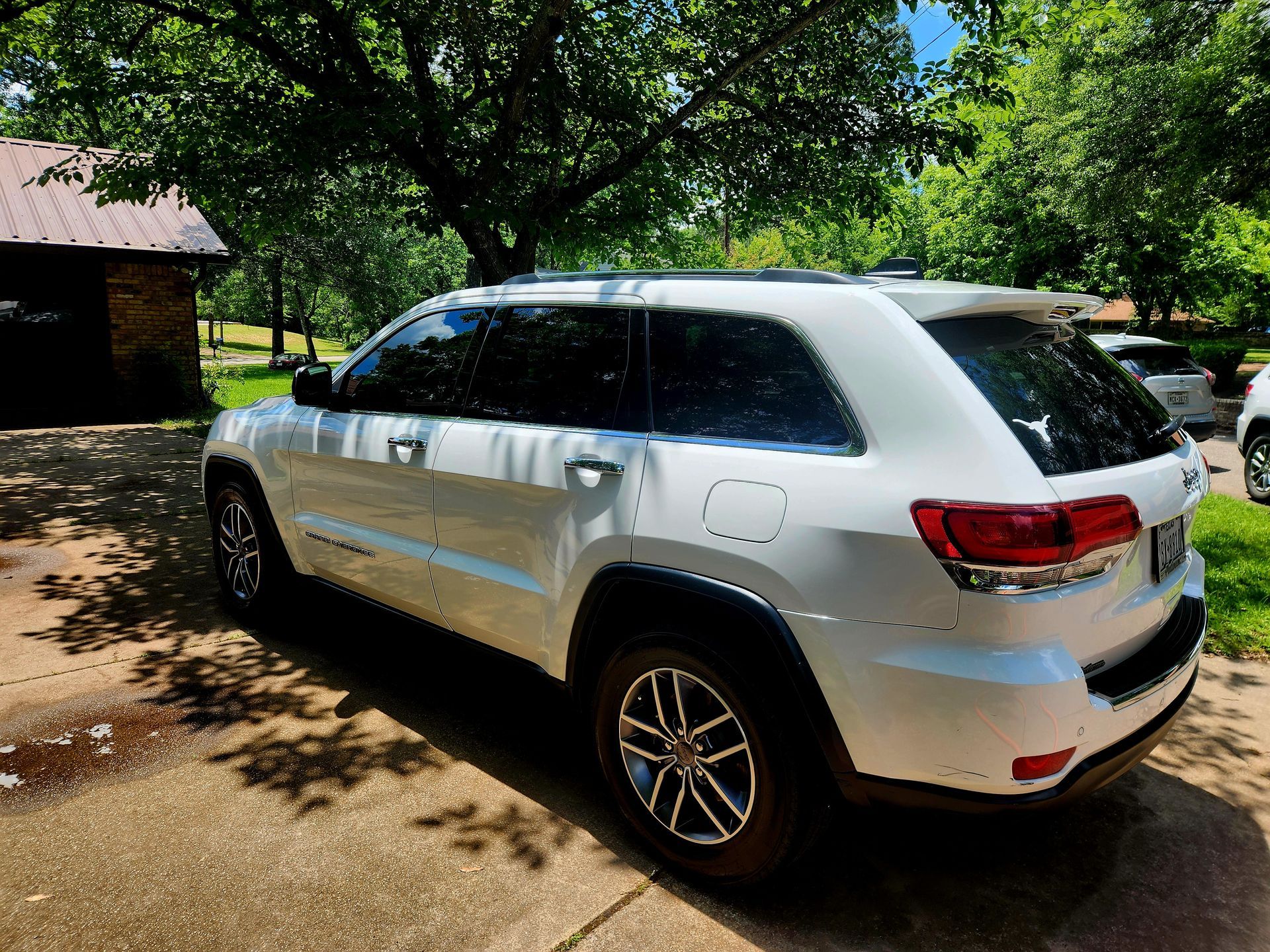 White Jeep Grand Cherokee parked on a concrete driveway, shaded by trees on a sunny day.