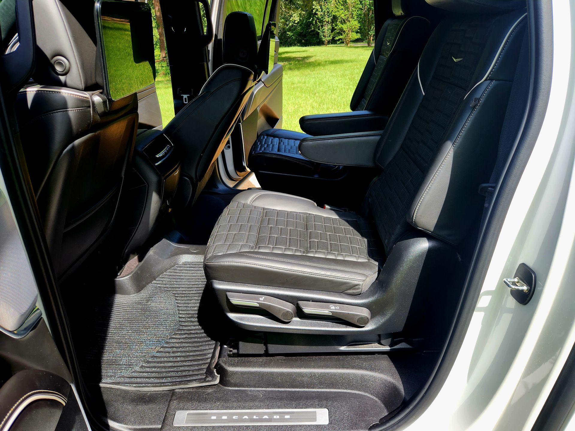 Interior view of a Cadillac SUV with black leather seats, a rubber floor mat, and a grassy background.