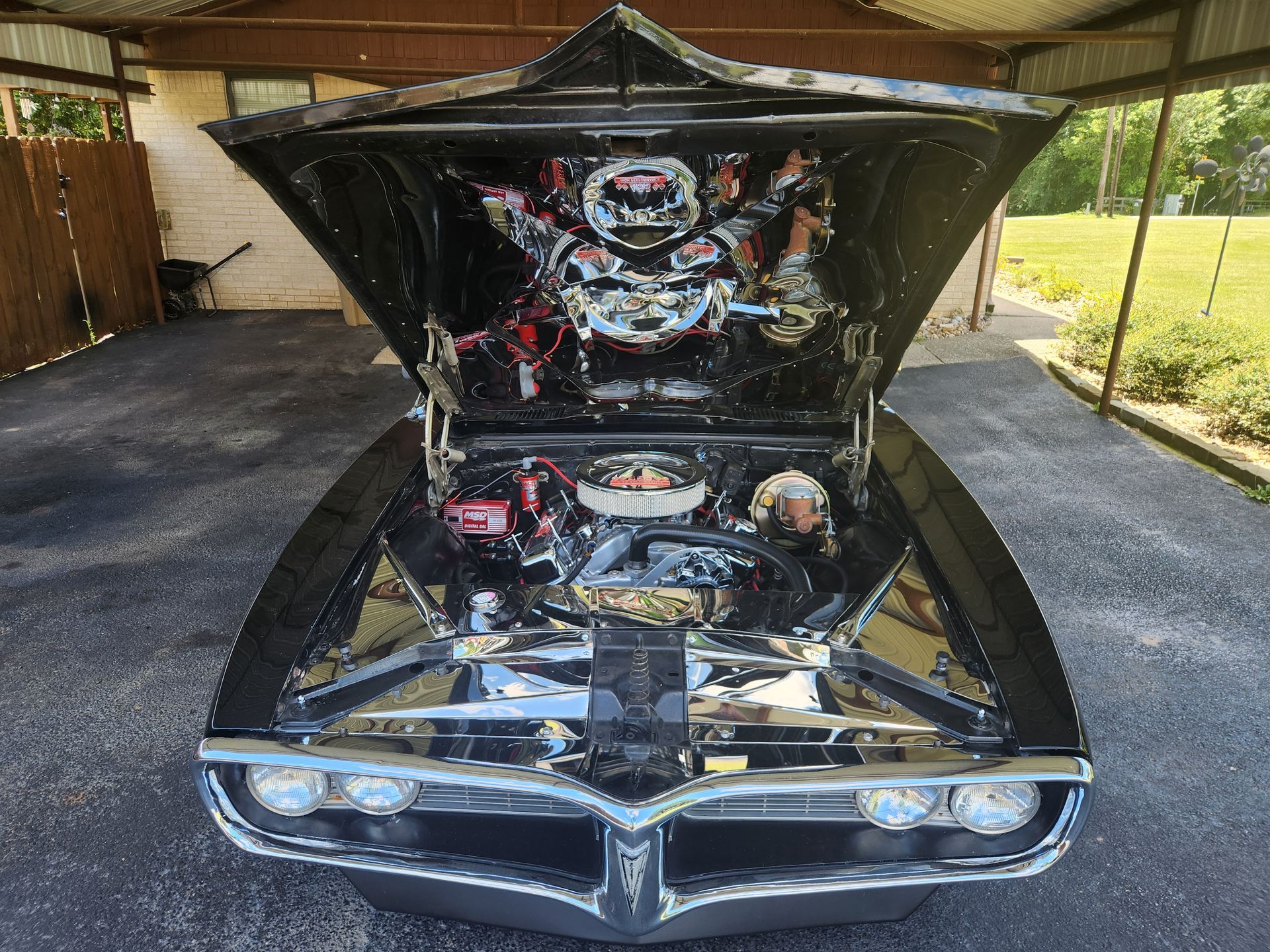 Black vintage car with hood open, engine visible, parked on a driveway.