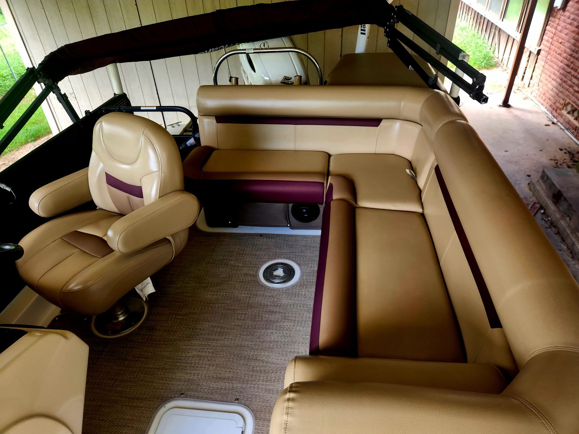 Tan and burgundy pontoon boat interior with captain's chair and wraparound seating.
