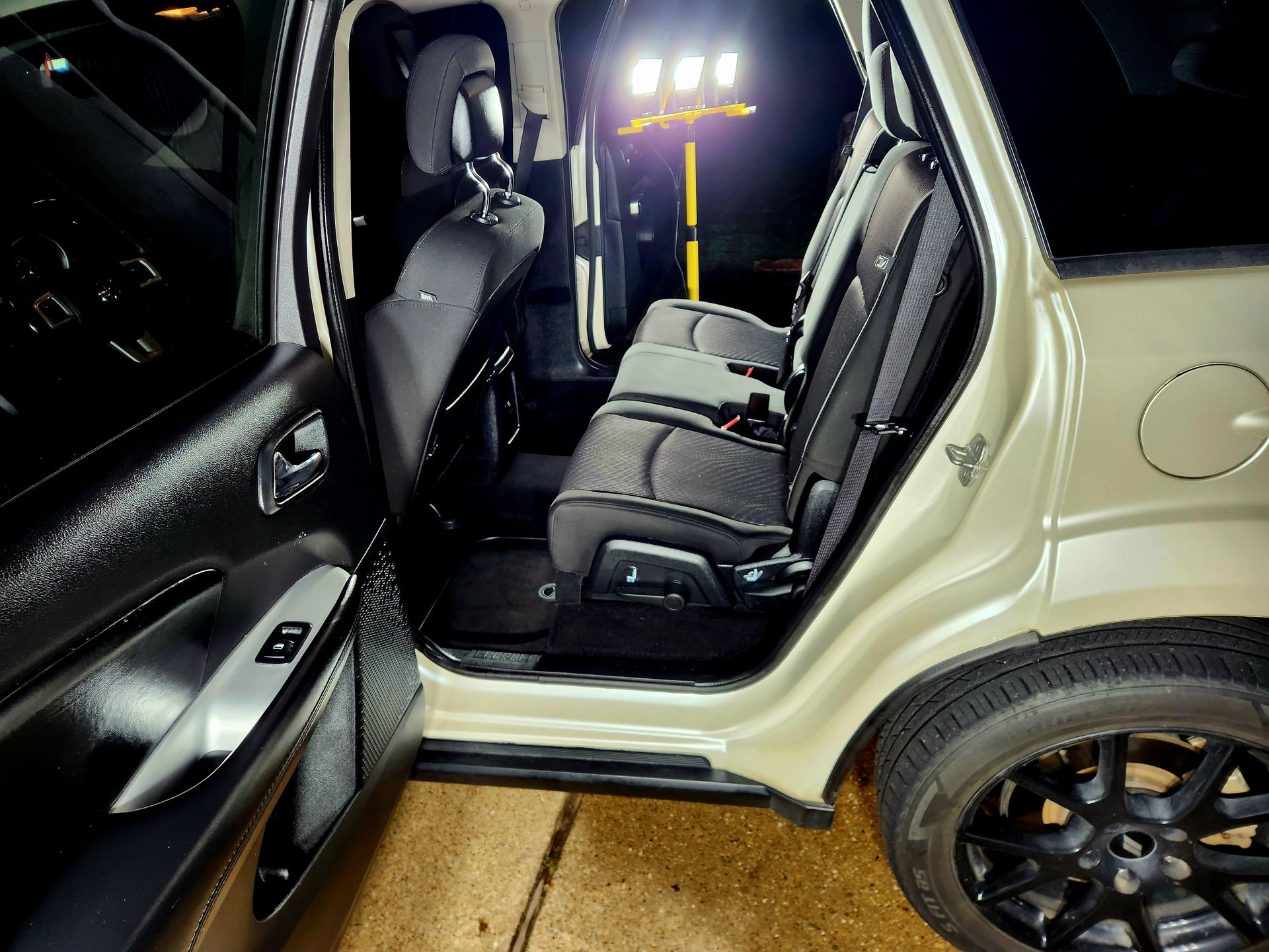 Interior of a tan SUV, open door reveals black second-row seats, black wheels, and a bright light behind.