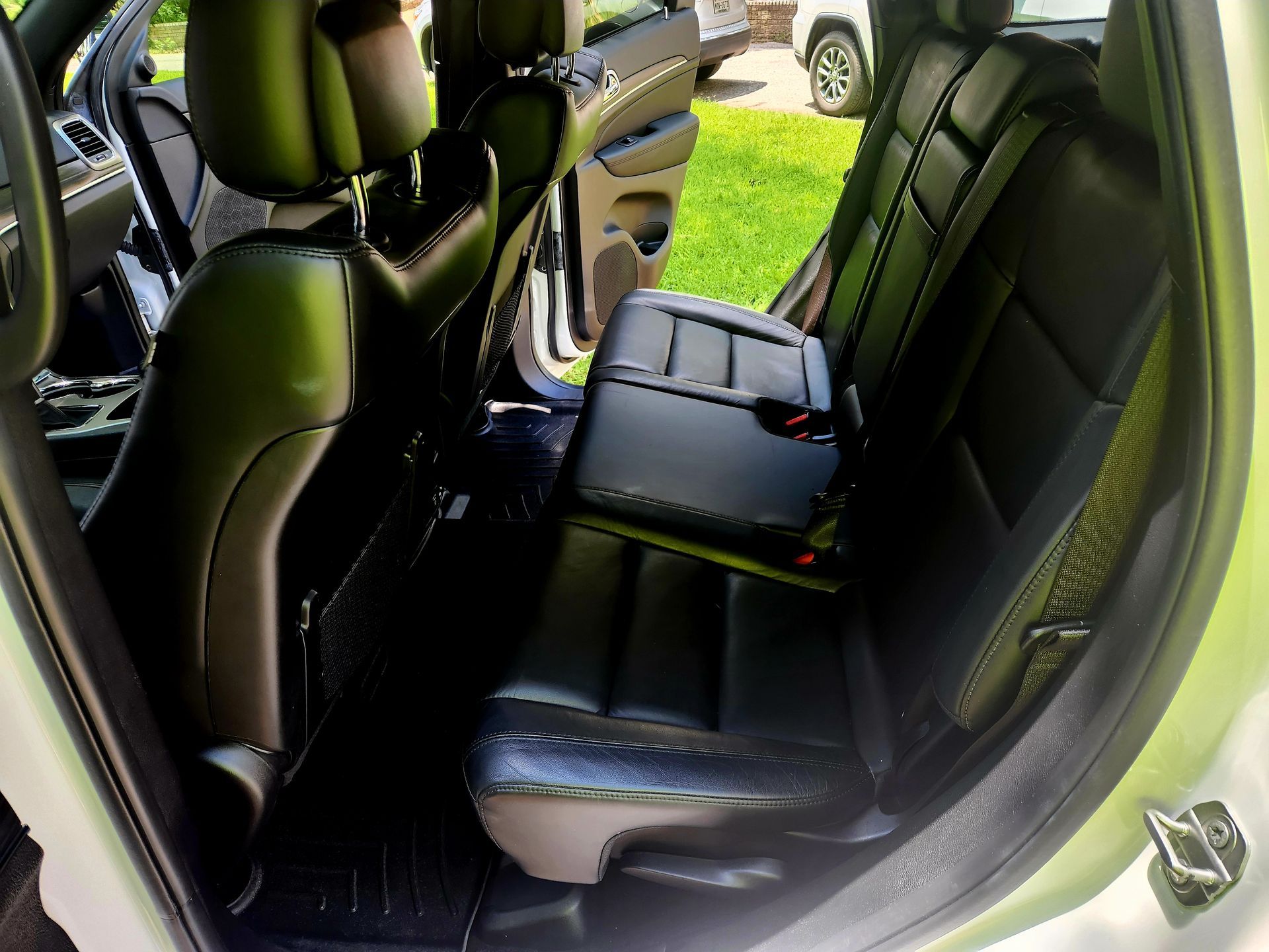 Black leather car seats in a vehicle. Back seat folded up, door open.