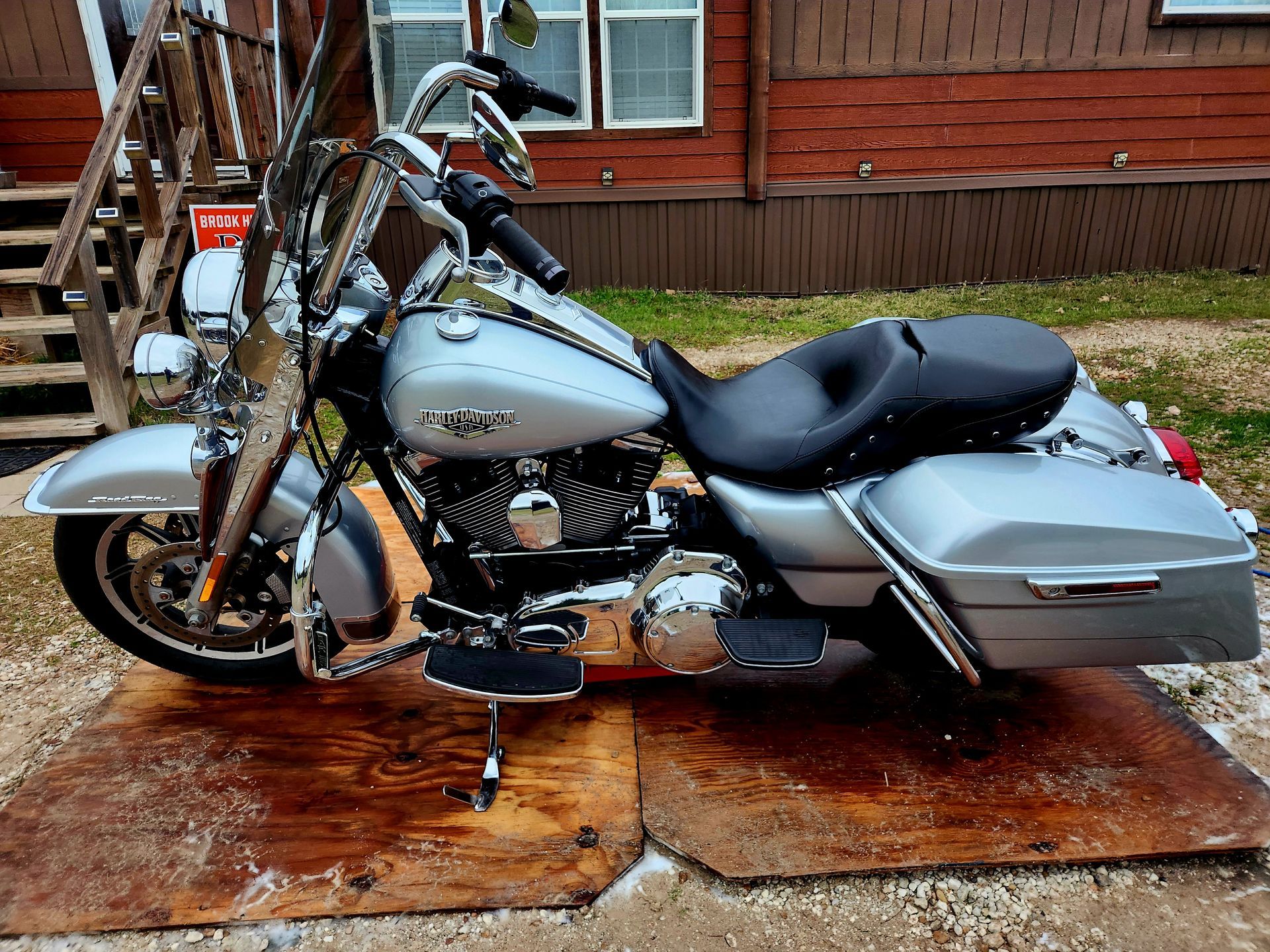 Silver Harley-Davidson motorcycle parked on wooden planks. Brown building in background.