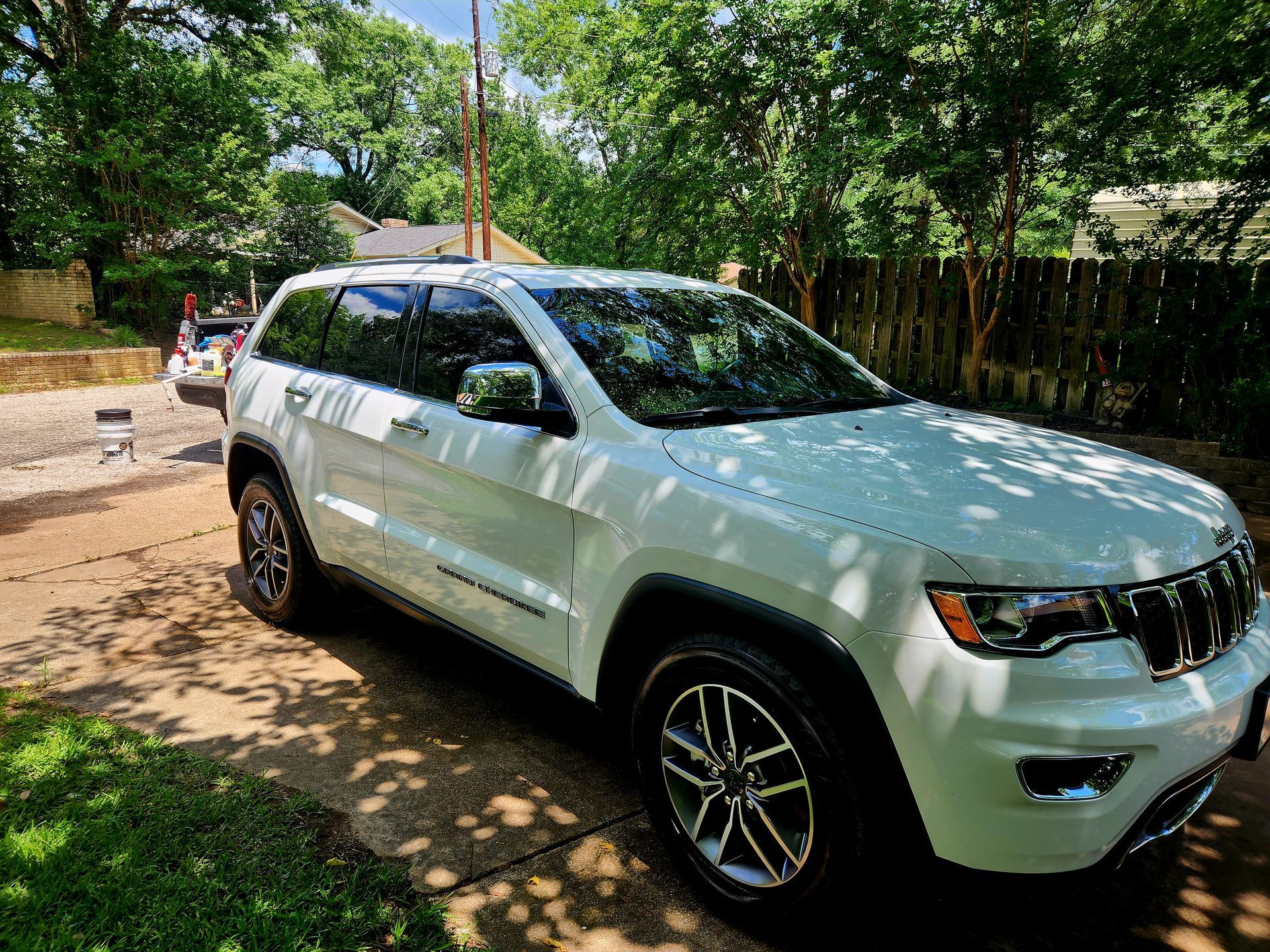 White Jeep Grand Cherokee parked on a driveway, surrounded by trees.